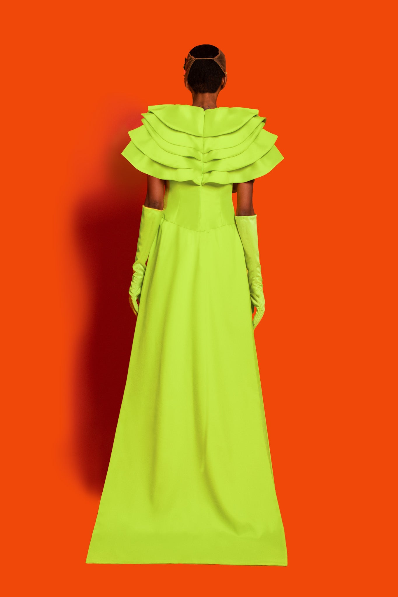 A lime green dropped waist maxi dress features exploded ruffles on the chest to shoulder and back with a buttcape.