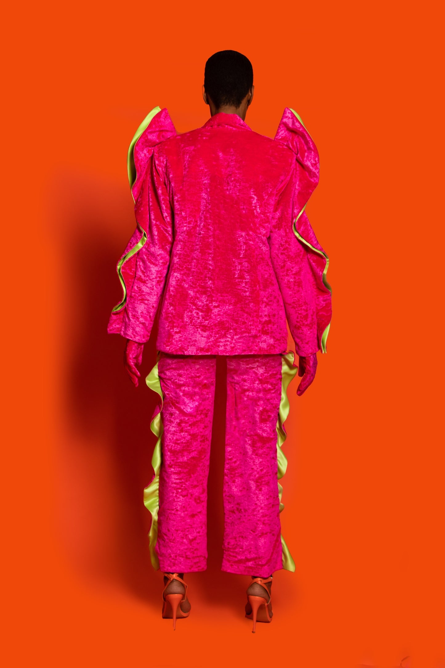 Back View.Fuchsia velvet tailoring pants feature ruffles on both sides and green lining.