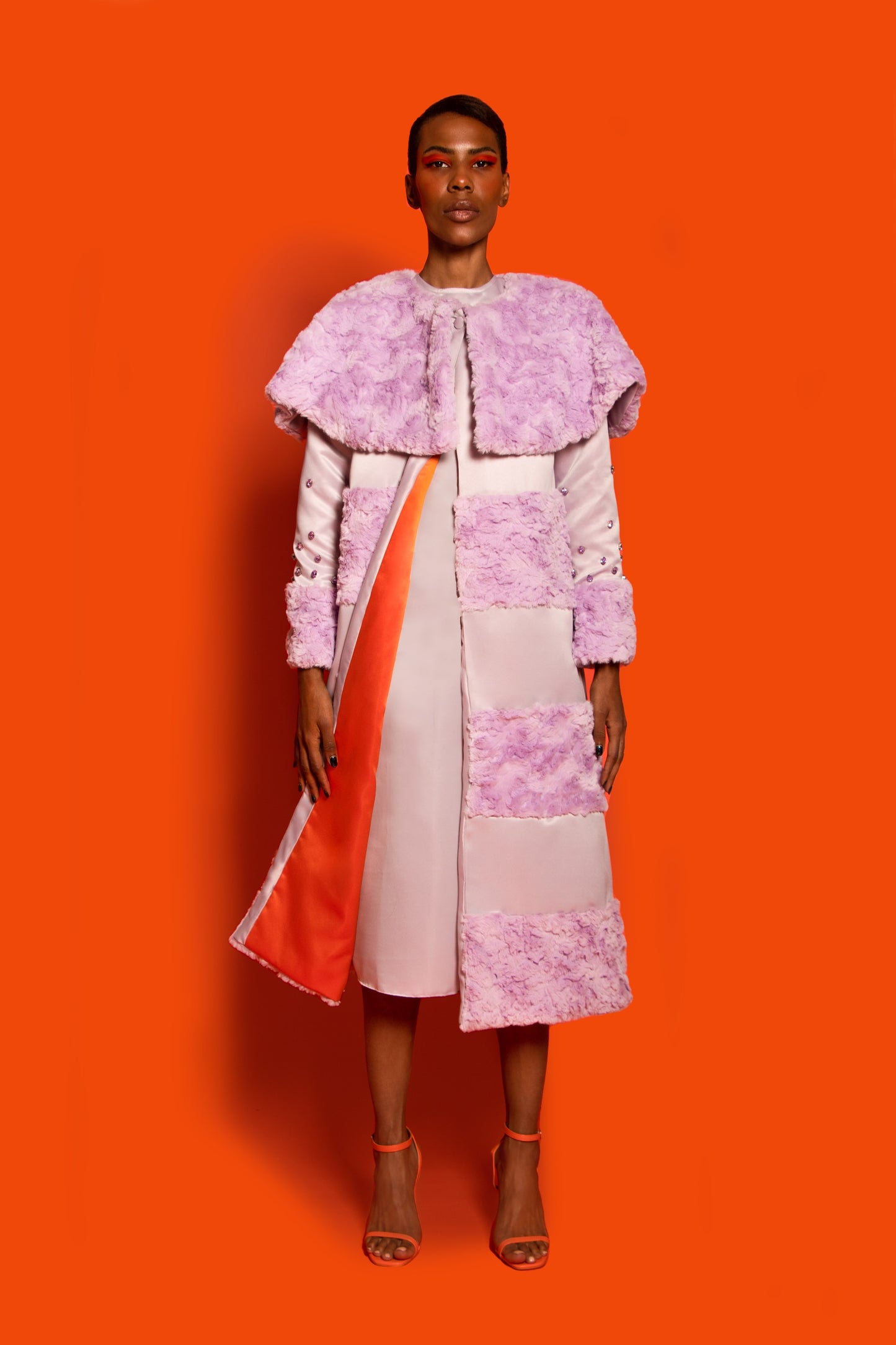 Front View. A light purple raccoon coat with faux fur and taffeta features embellished crystal sleeves and orange lining.