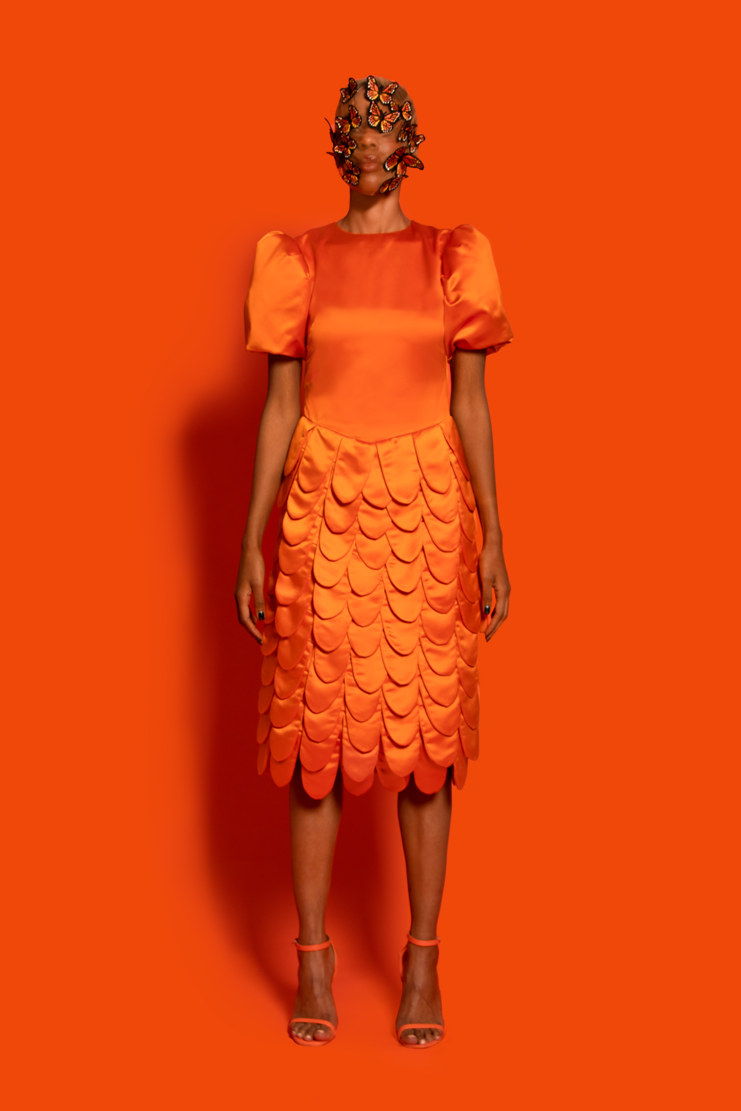 Front view.An orange silk taffeta midi dress features a puffy sleeve, dropped waist, and round shapes layers finished with silk lining.