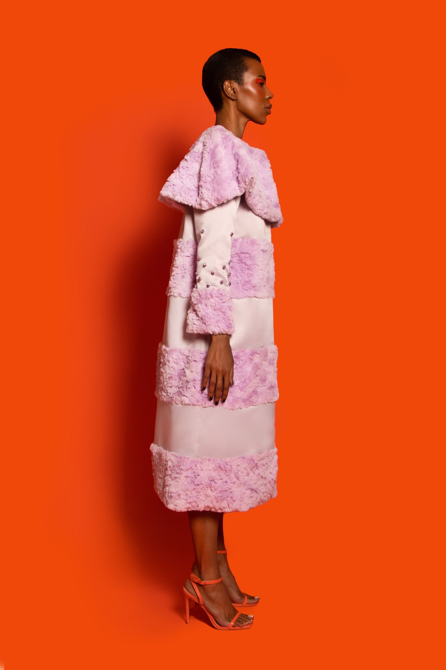 Side View.A light purple raccoon coat with faux fur and taffeta features embellished crystal sleeves and orange lining.