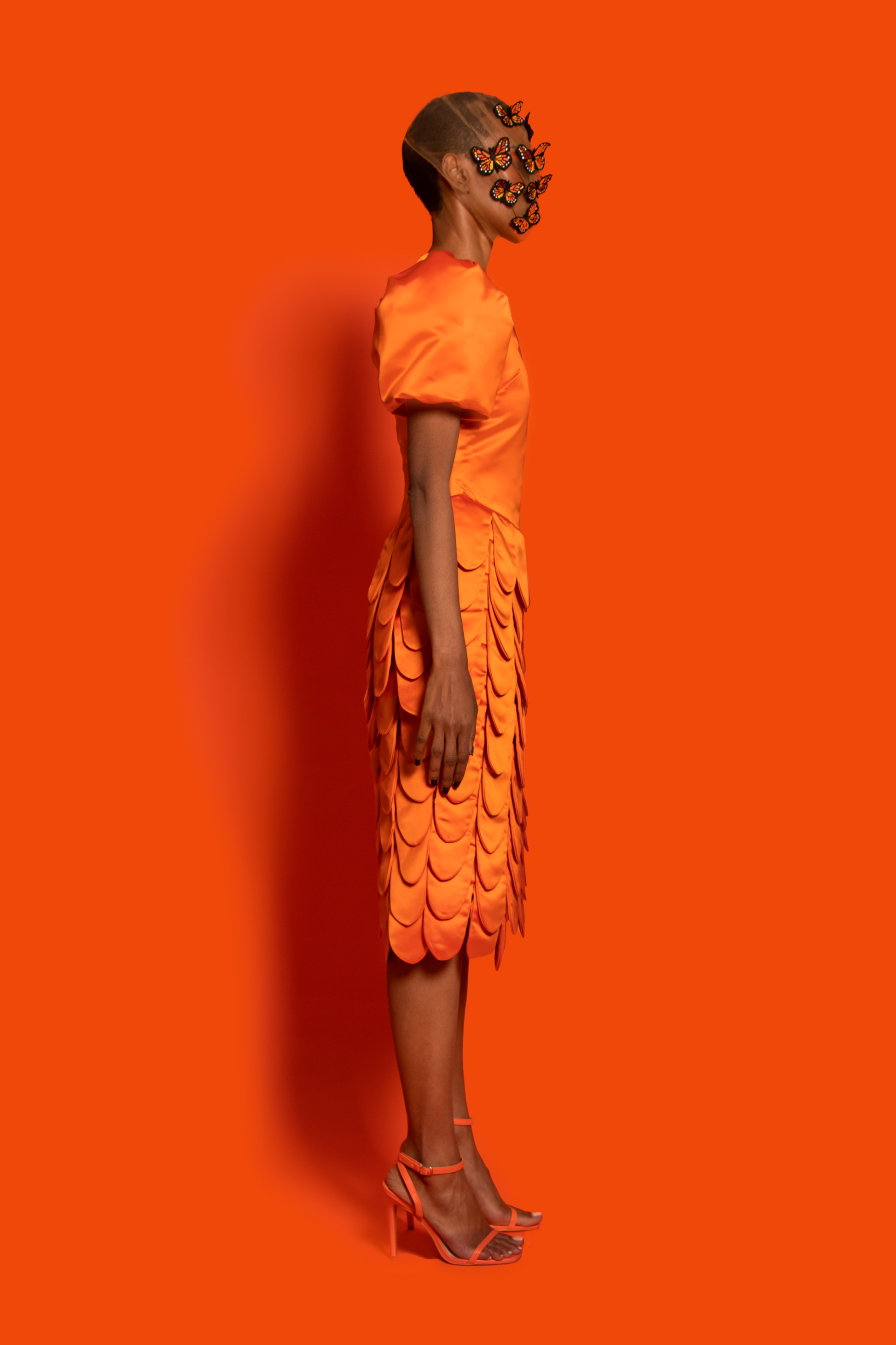 Side view. An orange silk taffeta midi dress features a puffy sleeve, dropped waist, and round shapes layers finished with silk lining.